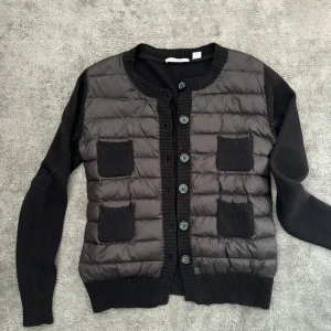 Svart jacka med knappar - jätte fin cardigan i 90 % cashmire och 10 % mohaire .En svart jacka med knappar framtill. Jackan har långa ärmar och två fickor på framsidan. Den är quiltad på framsidan och har ribbade muddar vid ärmslut och nederkant. 