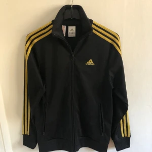 Svartgul Adidas tracktop - Jag säljer en svart adidas tracktop med gula streck. Tröjan är i bra skick. Tröjan är i barnstorlek 164 men funkar även som XS.