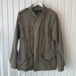 Filippa K Army jacka  - Army jacka från Filippa K. Jackan är grön, har knäppning och dragkedja där fram. Samt snörning i midjan som gör det möjligt att justera passformen. Ej fodrad. Så perfekt till vår / sommar / höst. Storleken är small (herr) men funkar bra på dam också.