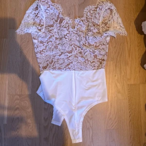 En vit body med spets  - En vit kottarnas body med spets, det är ett hudfärgat undertyg så man ser inte igenom, aldrig använd 