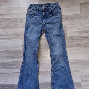 Ett par blå jeansbyxor med bootcut-stil. Byxorna har en klassisk femficksdesign och är tillverkade i denim. Från Polarn O Pyret i storlek 134