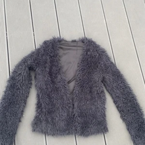 Svart lurvig kofta - Den är väl använd men har inga större fel förutom det ”rivmärket” man kan se på tredje bilden. Den är helt svart men ljuset gjorde att den ser mer grå ut