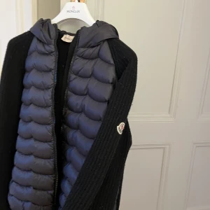 Stickad cardigan med din från Moncler - Moncler strlk 14 år men passar mig som är 170 cm. Svart med puffig luva i jättebra skick!