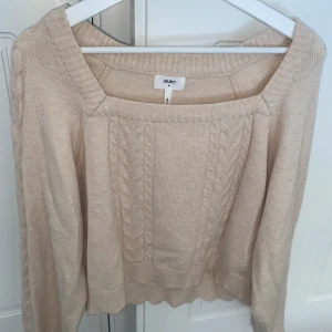 Stickad tröja - Beige stickad tröja med fyrkantsringning och vågliknande detaljer vid ärmar och midja. Endast använd en gång så som ny.