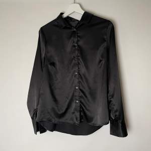 En svart ”silkesskjorta” från bikbok. Material: 95% polyester 5% elastisk.  Använd, men fin. Finns små skavanker på ena armen och längst ner på baksidan, men märks inte när man använder den.  Köparen står för frakten. Går att få spårbart.  Storlek S