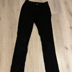 Svarta byxor med en slit vid ankeln  - Svarta byxor som passar en storlek större  Knapp och dragkedja fungerar utmärkt bra. Har 2 bakfickor.