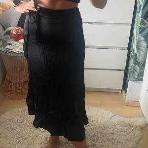 Svart satinkjol  - Så himla fin svart snedskuren satinkjol. Den har dragkedja på sidan och man knyter även rosett på sidan.  Midilängd Väldigt skrynklig på bilderna men går att lösa snabbt om man stryker med vattenånga! 