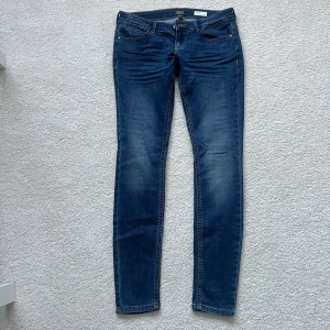 Lågmidjade Jeans - Blåa lågmidjade jeans i nyskick från ONLY ”Blue Denim anne 1995”. Coral Super Low Skinny. Använda 2 gånger. Storlek 27/30 ,ordinare pris 449
