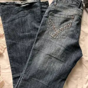 Mörkblåa lågmidjade jeans med glitter på fickorna. Supersnygga!! De är i bra skick utan lite slitningar längst ner på benen. Bilderna är tagna i olika ljus, men den andra bilden visar tydligast vilken färg jeansen är. 