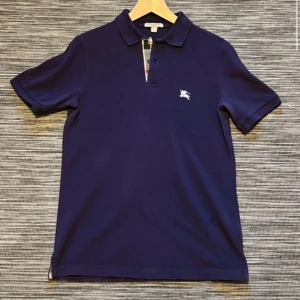 Burburry piké - Säljer en autentisk burburry piké. Blå/ lila färg,skick 9,5/10. Passar dig mellan 170-180.Nypris runt 4000-5000kr. Vid frågor/funderingar eller fler bilder är det bara att skriva!👍