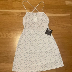 Miniklänning med band - Supersöt miniklänning i vit med blåa blommor. Knyts förslagsvis som på bild 2 i ryggen. 🦋 Stretchigt material samt resår bak runt midjan. Lite genomskinlig.