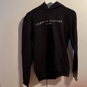 Svart Tommy hoodie - En svart tommy hoodie i stl 176 8/10 på skicket! Priset sitter ej i sten och bara att skriva vid funderingar!