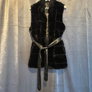  Pälsväst - Svart väst i fuskpäls med snyggt midje bälte i skinnimitation! Köpt på New Yorker. Går att stänga. Super fint skick - aldrig använd!