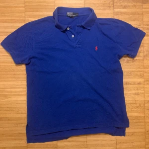 Ralph Lauren Piké blå - Fin Ralph Lauren piké. Helt perfekt skick förutom ett litet hål bakom kragen (se bild 3) men det är inget man tänker på. Det står att storleken är i L men den passar på mig som bär storlek M. Pm för fler bilder!