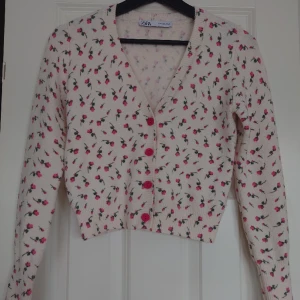 Söt kofta från Zara - Storlek S. Har hängt i garderoben sedan jag köpte den, så den är i jättefint skick!  Den är inte vit, offwhite, mot beiga hållet. Syns dåligt på bild. Rosa blommor och rosa knappar.