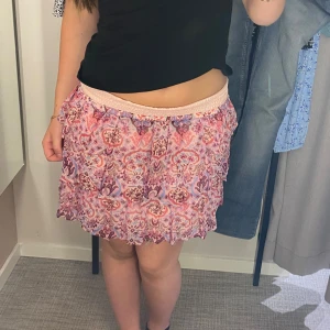 Mönstrad kjol från Lindex - Säljer en superfin mönstrad kjol från Lindex i storlek 158/164. Kjolen har ett färgglatt mönster i rosa, rött och blått och är perfekt för sommaren. Den har en elastisk midja som gör den bekväm att bära. Passar perfekt till både vardag och fest!