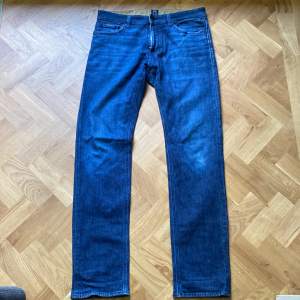 Säljer ett par snygga blå jeans från Hugo Boss. De är i bra skick och har en klassisk femficksdesign. Jeansen har en normal passform och är tillverkade i ett hållbart material. Perfekta för både vardag och fest! jeansen storlek är 34/34 men passar bra på mig som är 181 och väger 75kg 