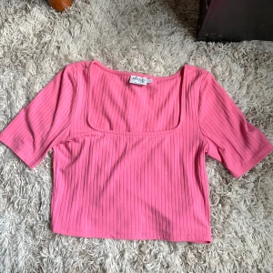 Rosa ribbad topp från NA-KD - Säljer en rosa ribbad topp från NA-KD. Den har en fyrkantig halsringning och korta ärmar. 