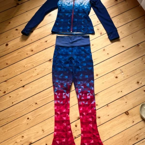 Blå och röd träningsset med geometriskt mönster - Säljer ett snyggt träningsset i blått och rött med geometriskt mönster. Tröjan har en dragkedja framtill och är långärmad. Byxorna är tighta och matchar tröjan perfekt. Materialet är mjukt och fleecefodrat på insidan, vilket gör det perfekt för kyligare dagar. Perfekt för träning eller bara för att chilla i. Storlek är dam M.