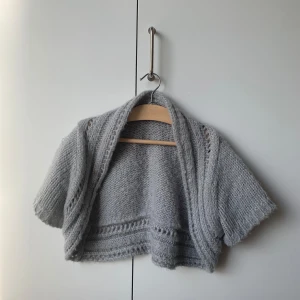 Kort kofta - Stickad kofta över endast axlarna. Har lite glitter i sömmarna. Står storlek 170 men passar XS/S 