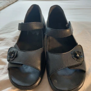 Pikolinos sandaler - Säljer ett par svarta sandaler i skinn med en söt blomdetalj på remmen. De har en justerbar rem runt ankeln för bättre passform och en bekväm sula som ger bra stöd. Sparsam använda. Perfekta för sommarens alla äventyr!