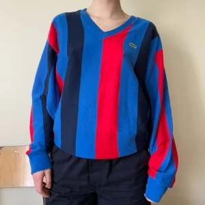 Stickad Lacoste Tröja  - Tunnare randig stickad tröja från Lacoste, producerad i Frankrike  I en sportig blå, mörkblå, röd och svart färgkombination. Bomull. Fint skick  Märkt som en storlek XL. Jag brukar ha storlek small överdelar. Har en bred mudd längs botten  