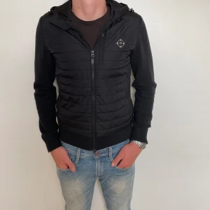 J Lindeberg Cardigan  - Säljer en J lindeberg Caridgan i storlek S, modellen är 185cm och väger 79kg, den är kort i midjan men bra i armarna på modellen. Ett litet hål i vänster innerficka men annars helt som ny!  Nypris:3000kr 