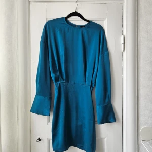 Klänning - Klänning från gina, använd en gång. Är mer grönblå i verkligheten och lite metallic i materialet. Sitter åt i kjol-delen och är mer löst sittande upptill. Längre ärmar. Säljer pga att den är för liten. 