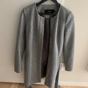 Grå kappa - Grå kappa från Vero Moda. Den har både knappar och dragkedja samt 2 fickor på utsidan. Med följer ett bälte