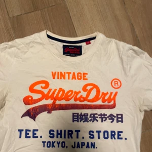 Superdry Vintage T-shirt - Vit T-shirt med orange och blått tryck. Fint skick. 