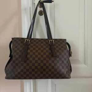 Damier Ebene Chelsea Tote Bag - LOUIS VUITTON  Bag  - Guldfärgade beslag - Brun damier ebene canvas med detaljer i brunt läder - Dubbel platt justerbar axelrem - Innerfoder i röd canvas med en dragkedjeförsedd innerficka - Vintage  Om du har ett prisförslag kan du gärna skriva till