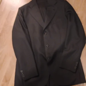 Kritstreck randig svart Herr kavaj med slits bak - Kritbitstreckig svart tung kavaj, aldrig tvättad, storlek 50, slits  bak i ryggen  Gjord av ylle 100 % köp hos stilkläder Kristianstad