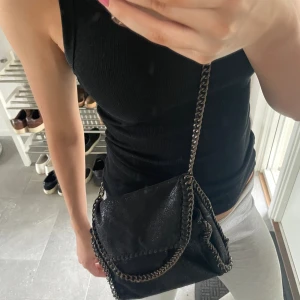 Stella McCartney liknande väska  - Säljer min svara axelremsväska med kedja i bra skick💕 kedjan har tappat färgen lite men inget man tänker på. Väskans har två fack varan ett med kedja