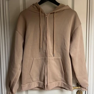 Beige hoodie  - En snygg beige huvtröja med dragkedja. Den har en ficka på magen och är i en avslappnad passform.