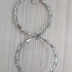 Silverfärgade örhängen - Ett par silverfärgade örhängen i form av ringar med ett vridet mönster. Örhängena har en enkel låsmekanism.köp via "Köp nu"