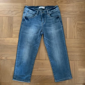 Blå trekvarts-långa jeans - Ett par blå trekvarts-långa jeans från Detroit by Lindex i storlek 158. Jeansen har en klassisk femficksdesign och är tillverkade i denim. De har en knapp- och dragkedjestängning framtill.