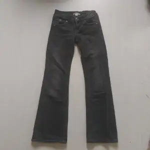 Bootcut jeans från Gina Tricot Young med låg midja. Jeansen är gråa och har utsvängda ben med fullängd. De har låg stretch, sömdetaljer framtill, bakfickor med knappar, dubbla knappar framtill och justerbar resår i midjan.