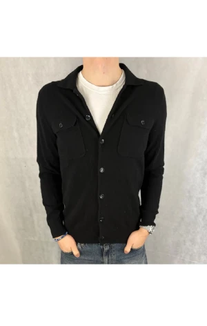 Svart cardigan i ull från Massimo Dutti - Svart skjorta från Massimo Dutti i mjuk ull. Långärmad och med en clean stil. Perfekt för dig som gillar minimalistisk stil och lyxigt material. OBS! En liten del på en knapp har blivit kantstött och tappat en liten del. DM för bild. Tveka inte att höra av dig.