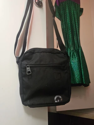 Svart axelväska från Björn Borg - Snygg svart axelväska från Björn Borg med justerbar rem och dragkedja framtill. Väskan har ett stilrent tryck med logga och flera fack inuti för smidig organisering. Perfekt storlek för mobil, plånbok och andra essentials.