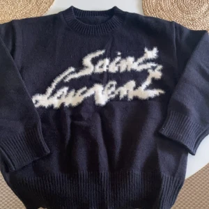 Svart Saint Laurent stickad tröja - Svart stickad tröja från Saint Laurent med vit, fuzzy logga framtill i cool graffiti-stil. Tröjan har rund hals, ribbade muddar och är långärmad. Perfekt för dig som vill ha en statement piece med lyxig känsla och street vibe. Hör av er vid funderingar och pris diskuterat ❤️✅💞🎉