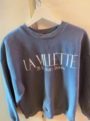 Blå sweatshirt från Gina Tricot - Säljer en blå sweatshirt från Gina Tricot i storlek M. Tröjan har trycket 'LA VILLETTE 211 Av Jean Jaurès' framtill, rund hals och ribbade muddar vid ärmslut och nederkant. Mjuk insida och långärmad modell, perfekt för chill dagar.