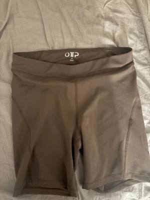 Bruna träningstights-shorts från OTP - Säljer ett par bruna, tighta träningstights-shorts från OTP i storlek M. De har hög midja och är gjorda i ett stretchigt syntetmaterial som sitter skönt på kroppen. Perfekta för gymmet eller löprundan.