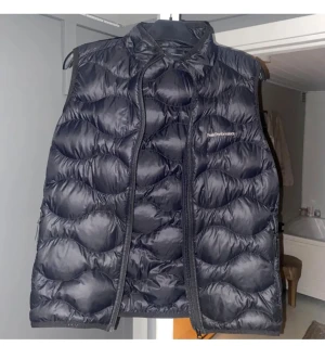 Svart dunväst från Peak Performance - Säljer en svart dunväst från Peak Performance, modell JR Helium Down Vest. Västen har quiltad design, hög krage och dragkedja framtill. Perfekt för lager-på-lager och riktigt snygg till både hoodie och t-shirt.