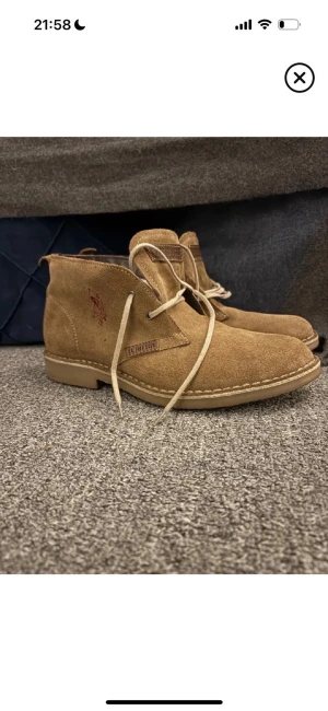 Beige mocka kängor från Polo Ralph Lauren - Snygga beige kängor från Polo Ralph Lauren i mjuk mocka med snörning och rund tå. Skorna har en platt sula i gummi och diskret broderad logga på sidan. Perfekt för dig som gillar klassisk stil med en modern touch.