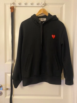 Svart hoodie Comme des Garçons Play - Svart hoodie från Comme des Garçons Play med klassisk röd hjärtlogga på bröstet. Hoodien är skön och enkel att styla, storleken är M men passar även S. Priset kan möjligtvis diskuteras. Skriv vid frågor eller önskemål om fler bilder. Tröjan är i jättebra skick!