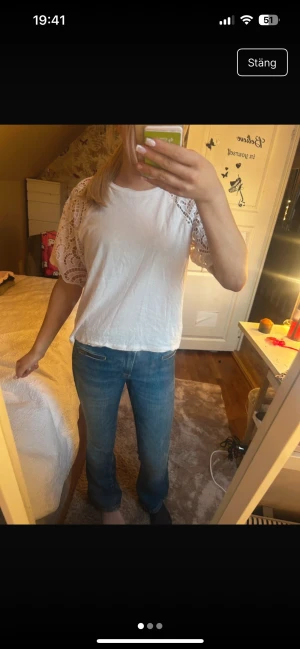 Vit blus med spetsärmar från LOW VISION - Vit blus från LOW VISION i storlek S. Toppen har korta, vida ärmar i vacker spets och en rak passform. Perfekt för dig som gillar en söt och stilren look med det lilla extra i ärmdetaljerna.