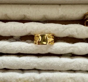 Bred guldpläterad ring med organisk form - Snygg bred ring i guldpläterad metall med coolt organiskt, vågigt mönster. Perfekt statement piece för dig som gillar unika detaljer och chunky smycken. Ringen har en blank finish som fångar ljuset och ger en lyxig vibe.