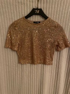 Glittrig set med topp och kjol  - Säljer en glittrig set med topp och kjol från Fashion Nova i skimrande guld med paljetter. Toppen är croppad. Kjolen har en rak och tight passform. Är i mycket bra skick och säljs i befintligt skick.