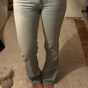 Ljusblå flared jeans från Zara - Säljer ett par ljusblå jeans från Zara i storlek 34. Modellen är flared, klassisk femficksdesign. Jeansen är tillverkade i denim med dragkedja och knapp framtill. Perfekt för dig som gillar retrovibbar och snygg passform.