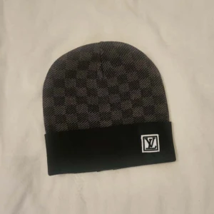  Rutig mössa i svart - Snygg mössa med klassiskt rutigt mönster i svart och mörk grått. Materialet är mjukt och känns lyxigt, perfekt för dig som gillar designeraccessoarer och inför vintern.